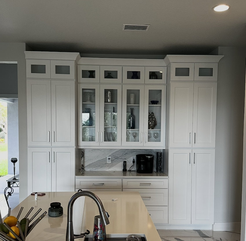 White Shaker coffee bar wall with tall pantry cabinets, glass-front uppers, a marble backsplash, and drawers below the counter